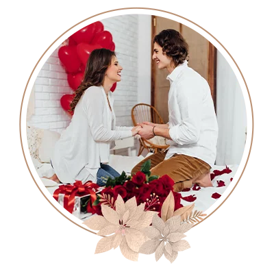 Happy couple holding hands, bouquet of red roses and gift box on the bed