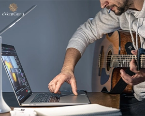 A man with a guitar in front of a laptop and earns to play